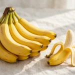 A bunch of ripe yellow bananas with one peeled banana beside them on a light cloth
