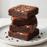 Stack of chocolate brownies with a crackly top on a plate