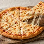 A cheese pizza on a wooden board with one slice being lifted away with a long cheese pull