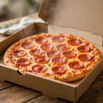 A whole pepperoni pizza in an open delivery box on a wooden table