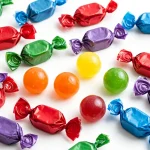 Colorful wrapped hard candies in red, green, blue and purple with unwrapped fruit candies on a white background