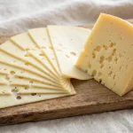 Slices of provolone cheese fanned out next to a wedge of provolone on a wooden board